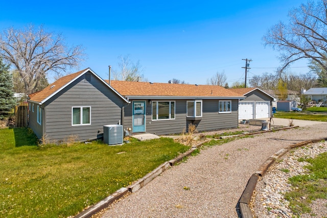 rear view of property with cooling unit, a detached garage, driveway, and a lawn