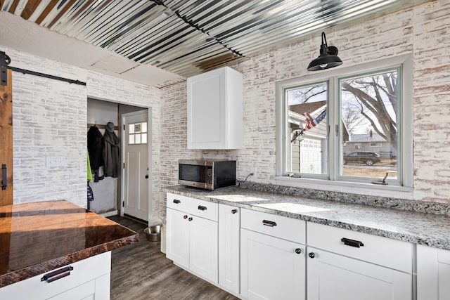 kitchen with white cabinetry, light stone counters, dark hardwood / wood-style floors, and brick wall