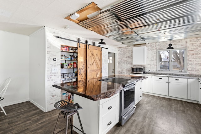 kitchen featuring appliances with stainless steel finishes, a barn door, dark wood-type flooring, white cabinets, and dark stone countertops