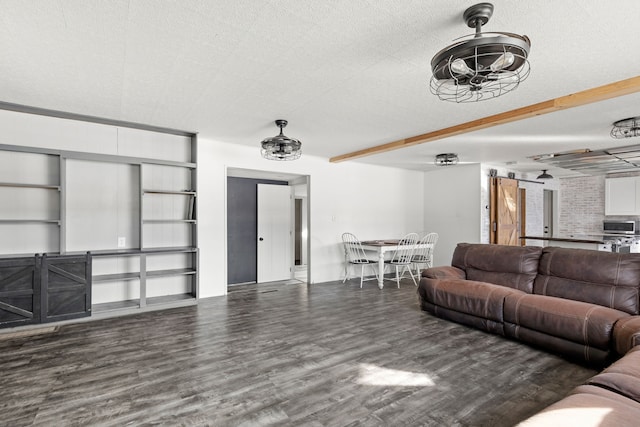 living room with beamed ceiling, a barn door, dark hardwood / wood-style flooring, and a textured ceiling