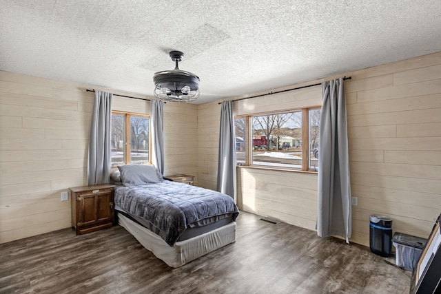 bedroom featuring wooden walls, dark hardwood / wood-style floors, and a textured ceiling