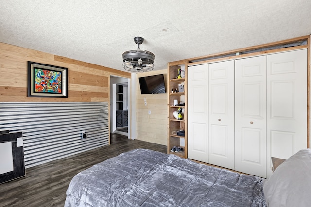 bedroom featuring dark wood-type flooring, a closet, wooden walls, and a textured ceiling