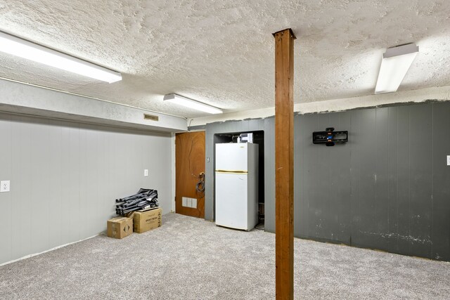 basement with light carpet, white fridge, and a textured ceiling