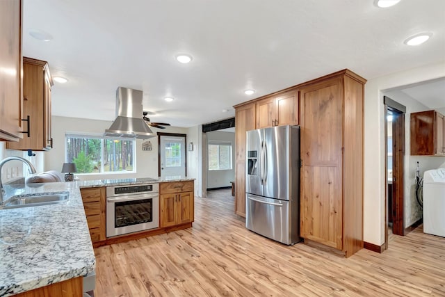 kitchen with island exhaust hood, appliances with stainless steel finishes, sink, and light hardwood / wood-style flooring