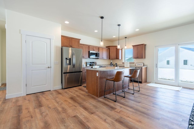 kitchen with a center island, hanging light fixtures, light wood-type flooring, appliances with stainless steel finishes, and light stone countertops