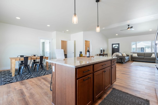 kitchen featuring hanging light fixtures, a center island, ceiling fan, light stone counters, and light wood-type flooring