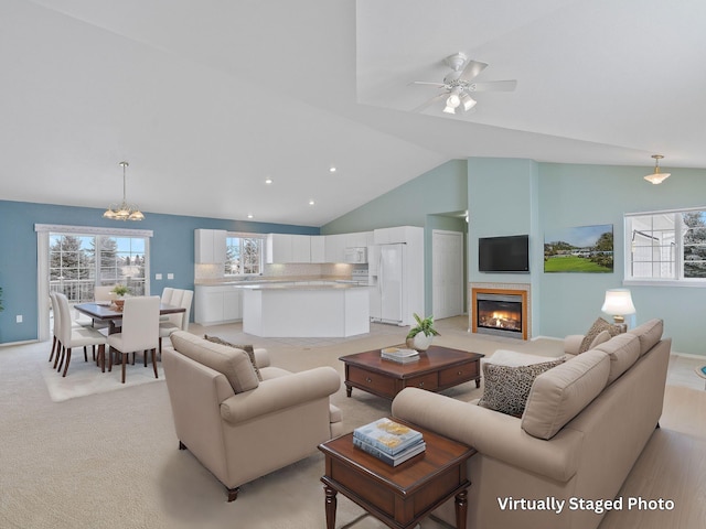 living room with ceiling fan with notable chandelier, light colored carpet, and high vaulted ceiling