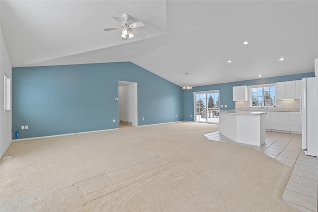 unfurnished living room featuring light colored carpet, lofted ceiling, and ceiling fan with notable chandelier