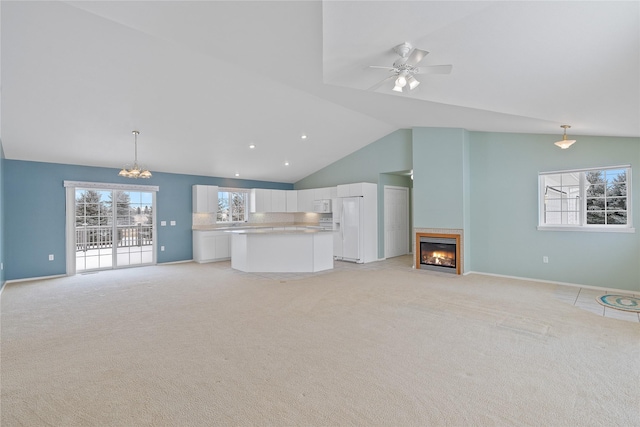 unfurnished living room with ceiling fan with notable chandelier, light carpet, and high vaulted ceiling