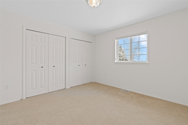 unfurnished bedroom featuring multiple closets and light carpet