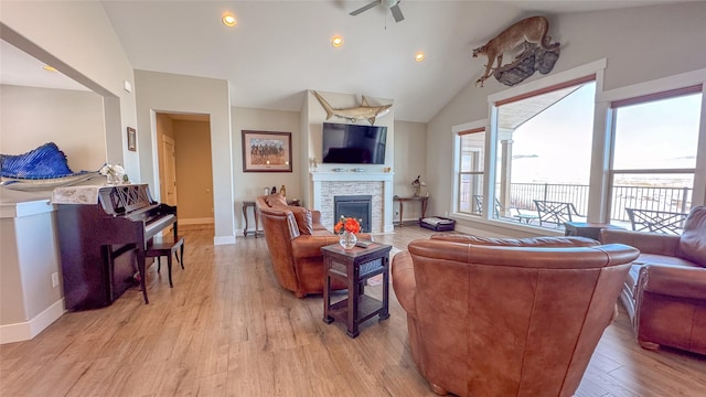 living room with a stone fireplace, lofted ceiling, ceiling fan, and light hardwood / wood-style flooring