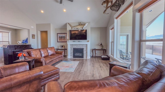 living room with high vaulted ceiling, a stone fireplace, a wealth of natural light, and light wood-type flooring