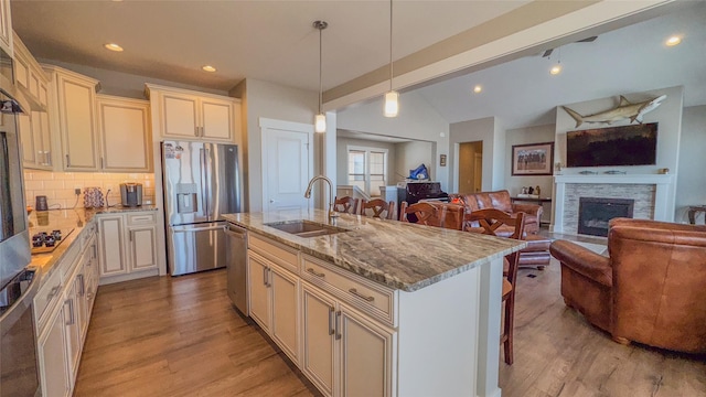 kitchen with sink, light stone counters, hanging light fixtures, an island with sink, and stainless steel appliances