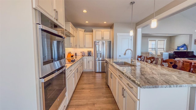 kitchen featuring sink, decorative light fixtures, stainless steel appliances, light stone countertops, and a kitchen island with sink