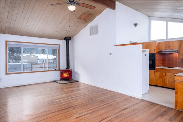 kitchen featuring pendant lighting, sink, backsplash, vaulted ceiling with beams, and a wood stove