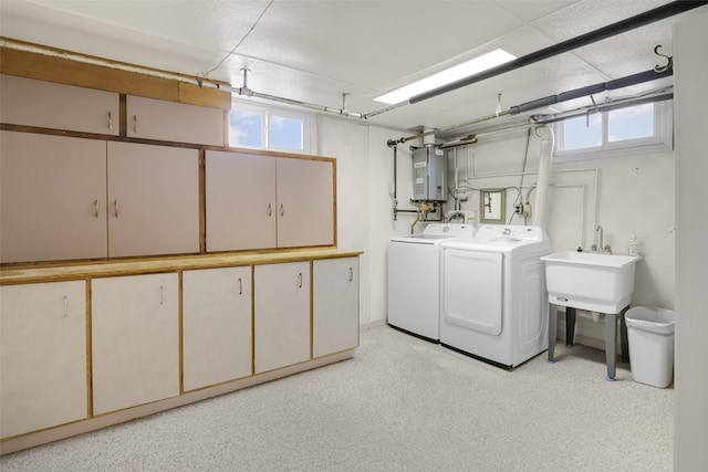 clothes washing area featuring cabinets, tankless water heater, sink, and washer and dryer