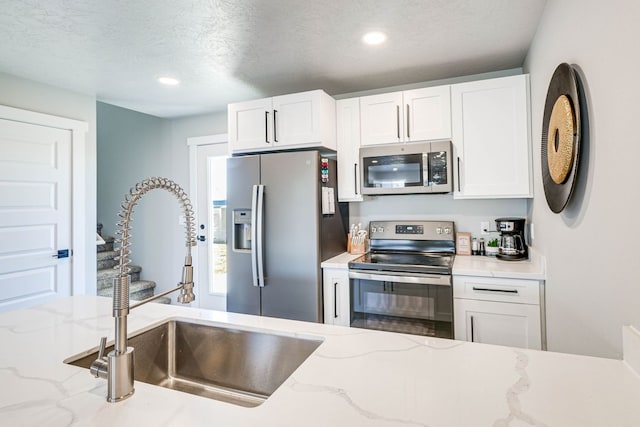 kitchen featuring sink, white cabinets, light stone counters, stainless steel appliances, and a textured ceiling