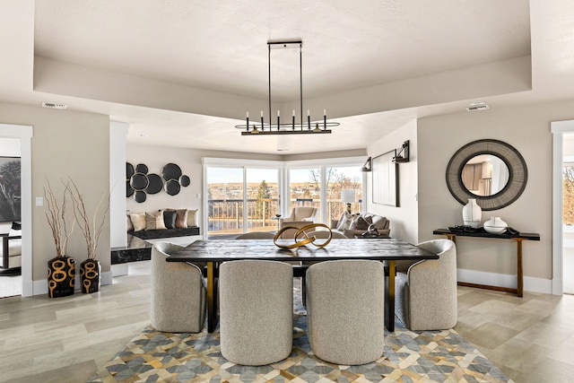 dining space with an inviting chandelier, a tray ceiling, and light wood-type flooring