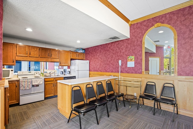 kitchen featuring sink, dark colored carpet, ornamental molding, white appliances, and a textured ceiling