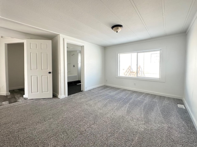 unfurnished bedroom featuring ensuite bathroom, a textured ceiling, and dark colored carpet