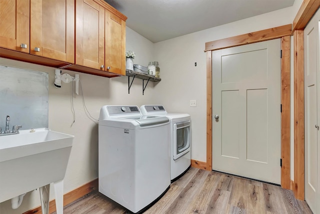 laundry room featuring light hardwood / wood-style floors, cabinets, washer and clothes dryer, and sink