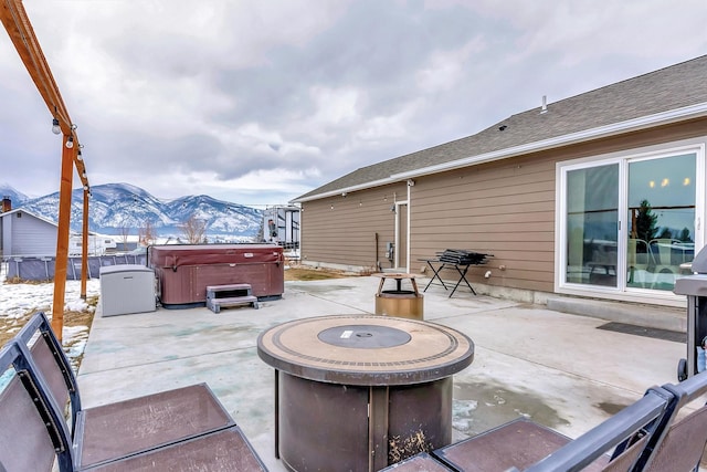 view of patio with a hot tub, a mountain view, and a fire pit