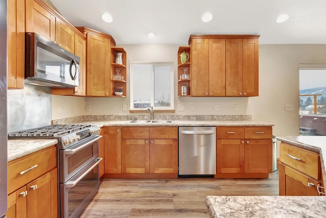 kitchen with light stone counters, sink, light hardwood / wood-style floors, and appliances with stainless steel finishes