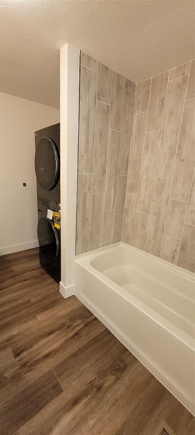 bathroom featuring wood-type flooring, a bathing tub, stacked washer and clothes dryer, and a textured ceiling