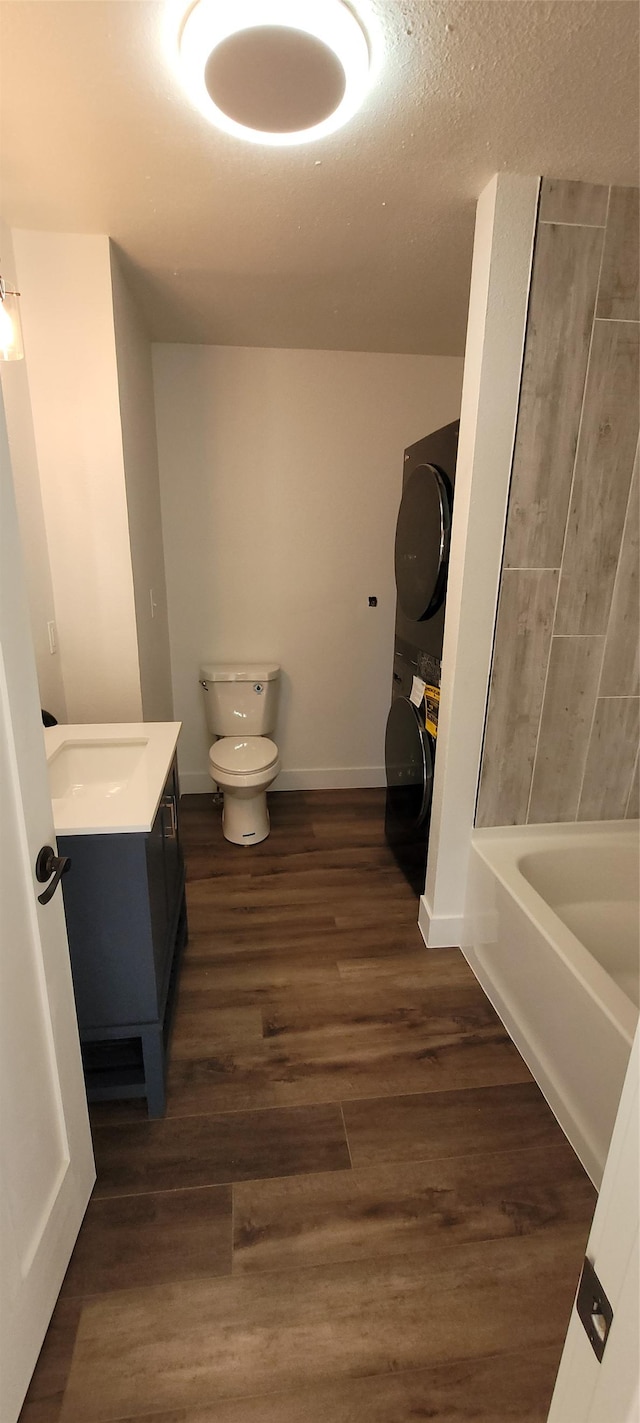 bathroom featuring stacked washing maching and dryer, wood-type flooring, vanity, toilet, and a textured ceiling