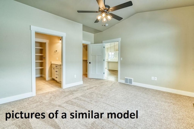 carpeted bedroom with a spacious closet, vaulted ceiling, ensuite bath, and ceiling fan