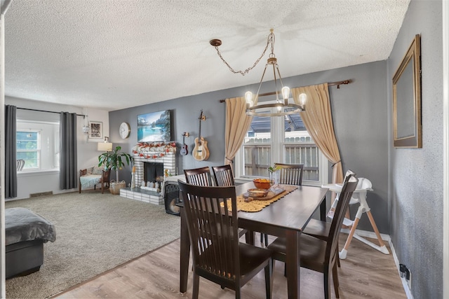 dining space with an inviting chandelier, a textured ceiling, a brick fireplace, and hardwood / wood-style flooring