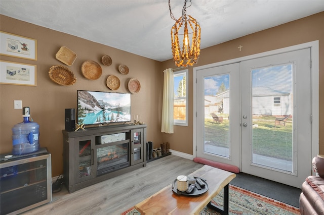 living room featuring french doors, a healthy amount of sunlight, a chandelier, and light hardwood / wood-style floors