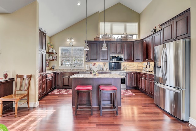 kitchen featuring light stone counters, appliances with stainless steel finishes, dark hardwood / wood-style floors, a kitchen island, and pendant lighting