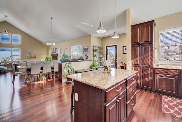 kitchen featuring dark wood-type flooring, a breakfast bar area, a center island, hanging light fixtures, and light stone countertops