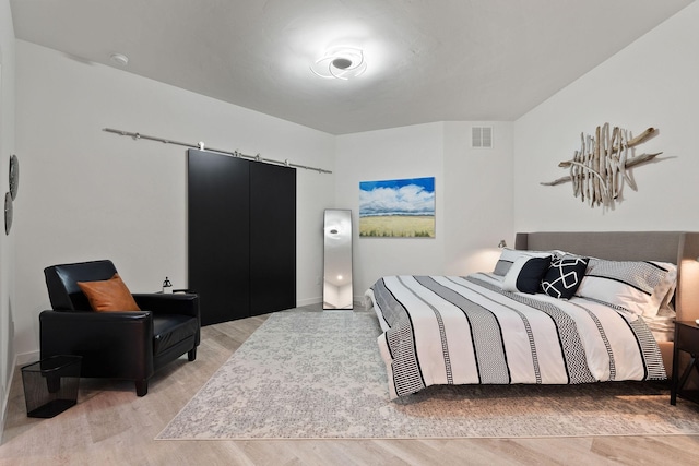 bedroom with a barn door and light hardwood / wood-style flooring