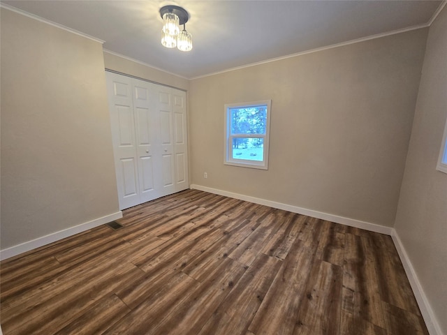 unfurnished bedroom with dark wood-type flooring, ornamental molding, and a closet