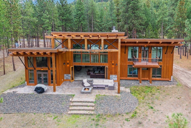1180 Reardon Ln, Alberton, MT 59820 - rear view of house with an outdoor living space with a fire pit, a patio area, french doors, a view of trees, and board and batten siding