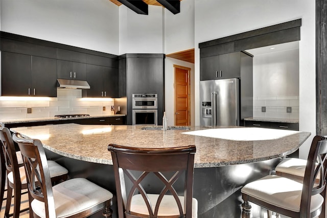 kitchen featuring sink, a kitchen breakfast bar, decorative backsplash, stainless steel appliances, and a center island with sink