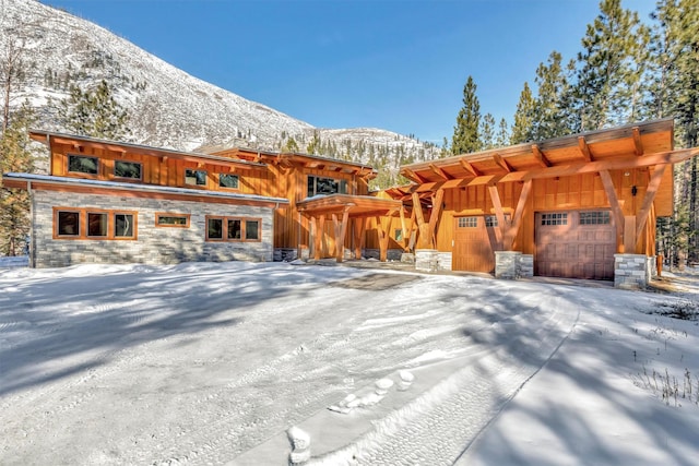 1180 Reardon Ln, Alberton, MT 59820 - snow covered property featuring stone siding, board and batten siding, a mountain view, and a garage