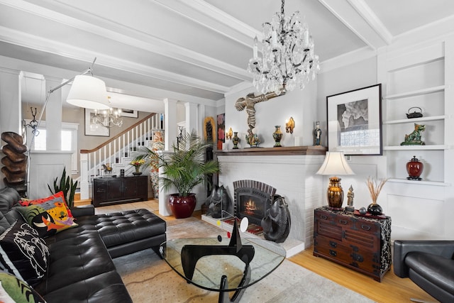 living room with beam ceiling, a brick fireplace, a chandelier, and light hardwood / wood-style floors