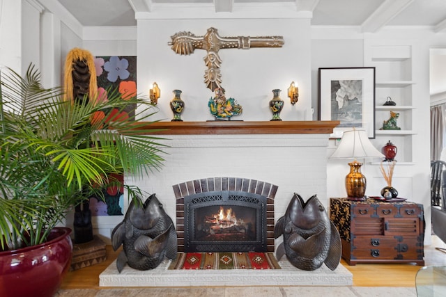 interior details with beamed ceiling, wood-type flooring, ornamental molding, a brick fireplace, and built in shelves