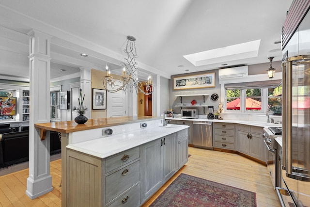 kitchen with hanging light fixtures, appliances with stainless steel finishes, gray cabinets, an island with sink, and light hardwood / wood-style floors