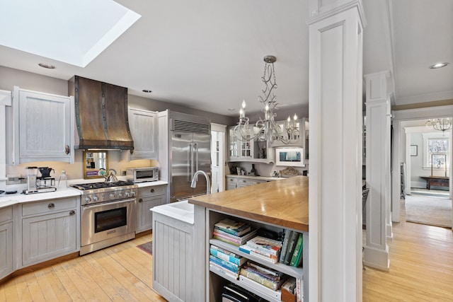 kitchen featuring premium range hood, hanging light fixtures, light wood-type flooring, high quality appliances, and gray cabinets