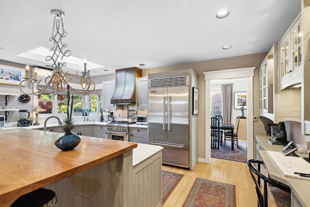 kitchen featuring gray cabinets, premium range hood, hanging light fixtures, high end appliances, and light hardwood / wood-style flooring