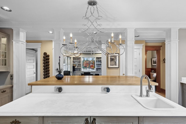 kitchen featuring sink, decorative light fixtures, a center island with sink, ornamental molding, and decorative columns