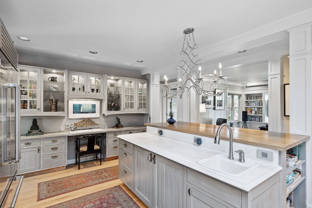 kitchen featuring pendant lighting, sink, gray cabinets, light hardwood / wood-style flooring, and a center island with sink