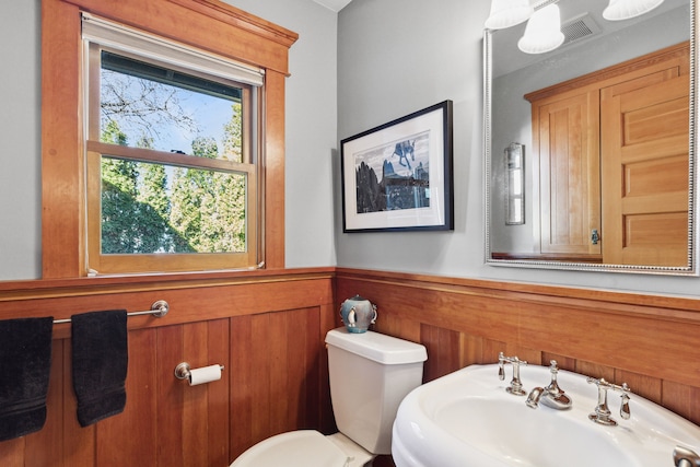 bathroom with sink, toilet, and wood walls