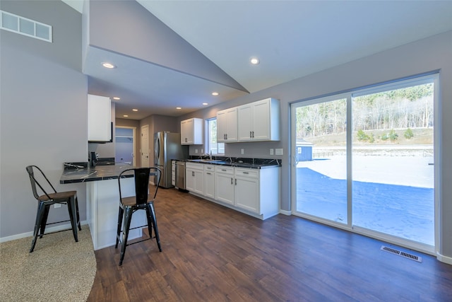 kitchen featuring lofted ceiling, sink, white cabinetry, appliances with stainless steel finishes, and a kitchen breakfast bar