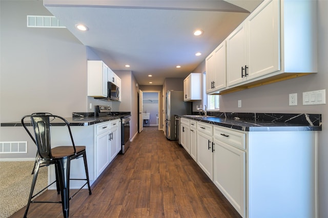 kitchen featuring white cabinetry, sink, a kitchen breakfast bar, stainless steel appliances, and dark wood-type flooring