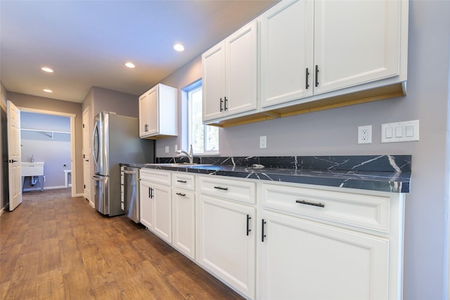 kitchen with sink, dishwasher, dark stone countertops, white cabinets, and dark hardwood / wood-style flooring